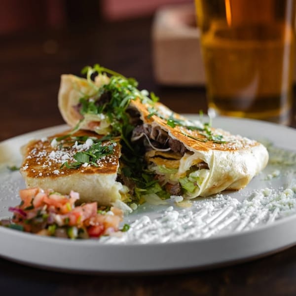A sliced Bien Y Tu burrito filled with meat and lettuce, served with pico de gallo.