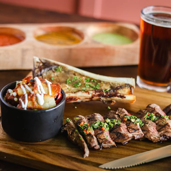 Mexican grilled steak, bone marrow, potatoes, and beer on a wooden board with sauces.