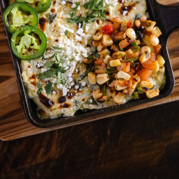 Bien Y Tu's Mexican esquites in a cast iron skillet, topped with cheese, cilantro, and jalapeños.