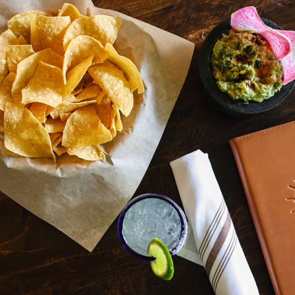 Bien Y Tu Mexican restaurant's chips, guacamole, margarita, and menu on a wooden table.