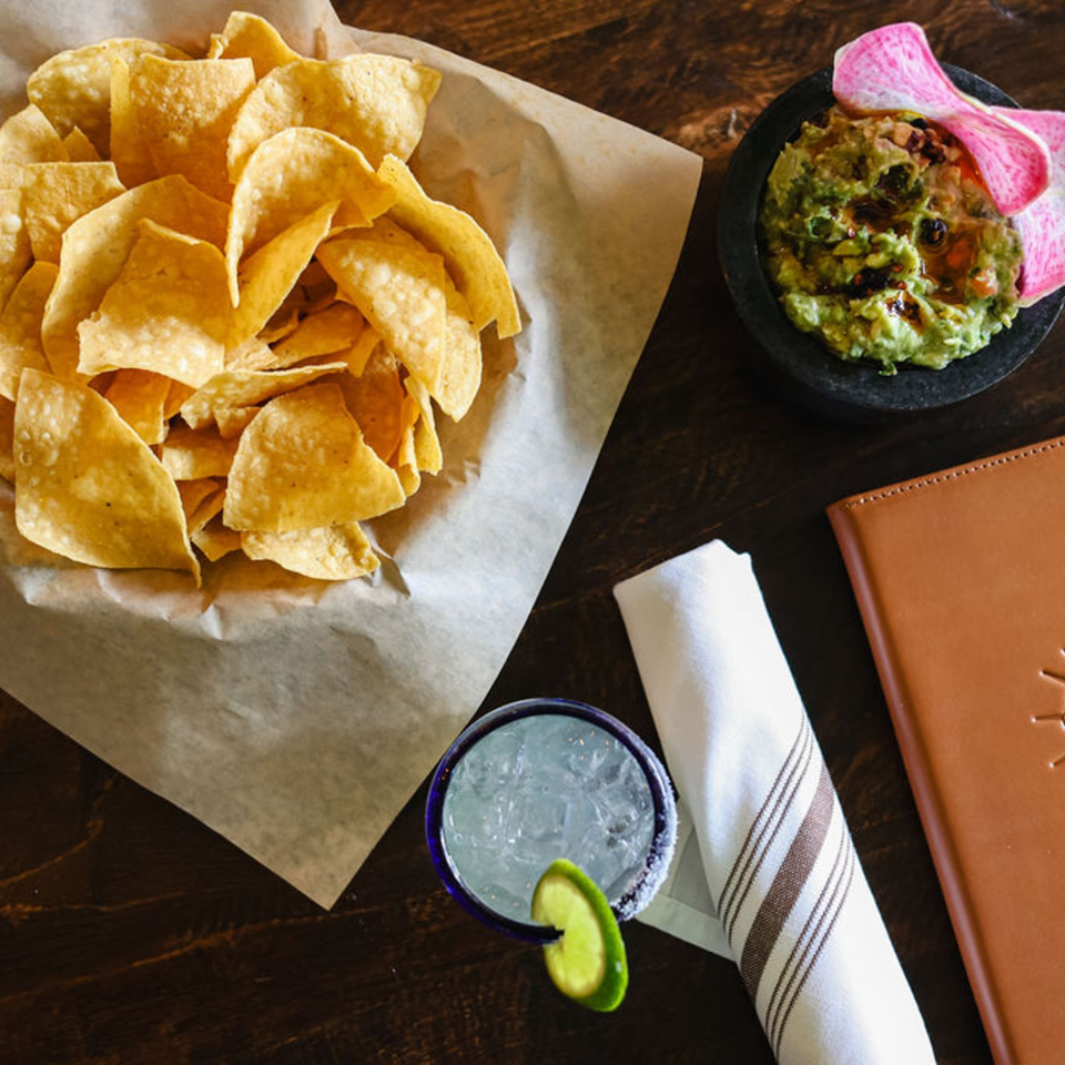 Bien Y Tu Mexican restaurant's chips, guacamole, margarita, and menu on a wooden table.