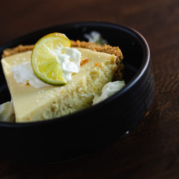 Slice of Key Lime Pie with whipped cream and a lime wedge in a black bowl.
