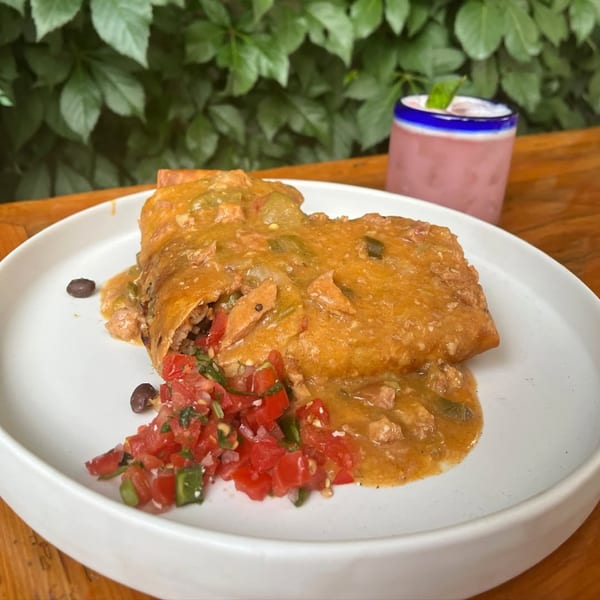 A Bien Y Tu Mexican burrito covered in orange sauce, with pico de gallo and a pink drink.