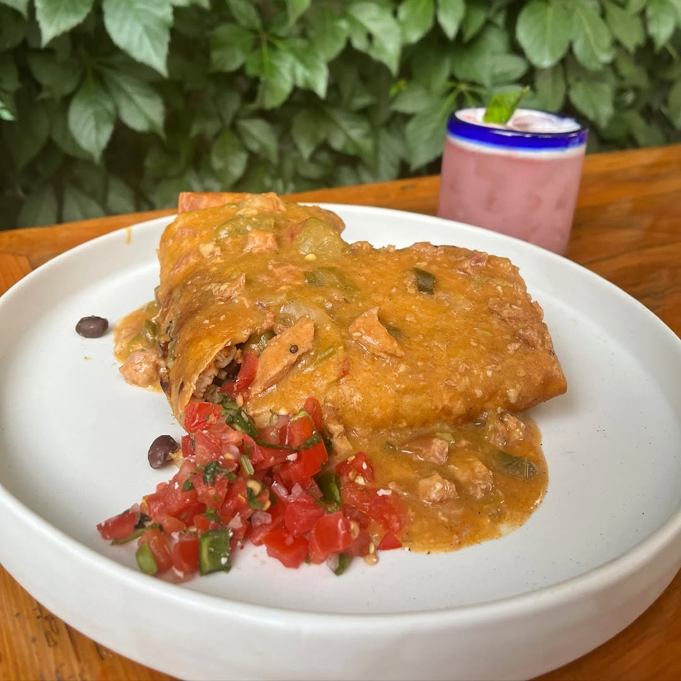 A Bien Y Tu Mexican burrito covered in orange sauce, with pico de gallo and a pink drink.